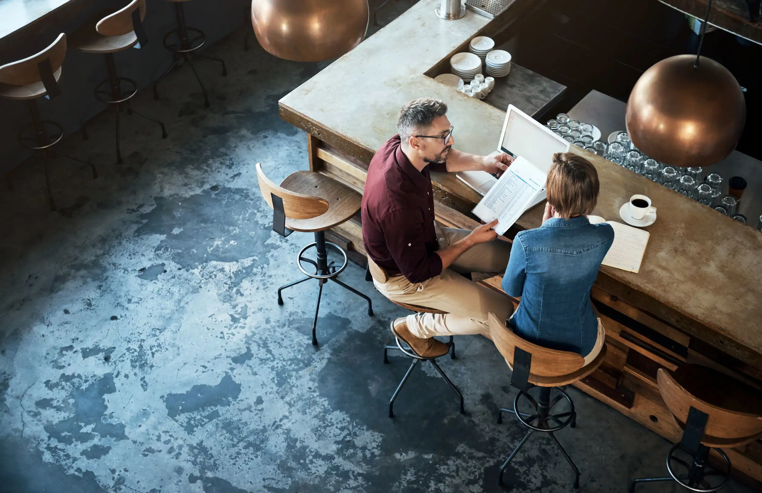 Two individuals seated at a bar, working on a laptop and going over documents.