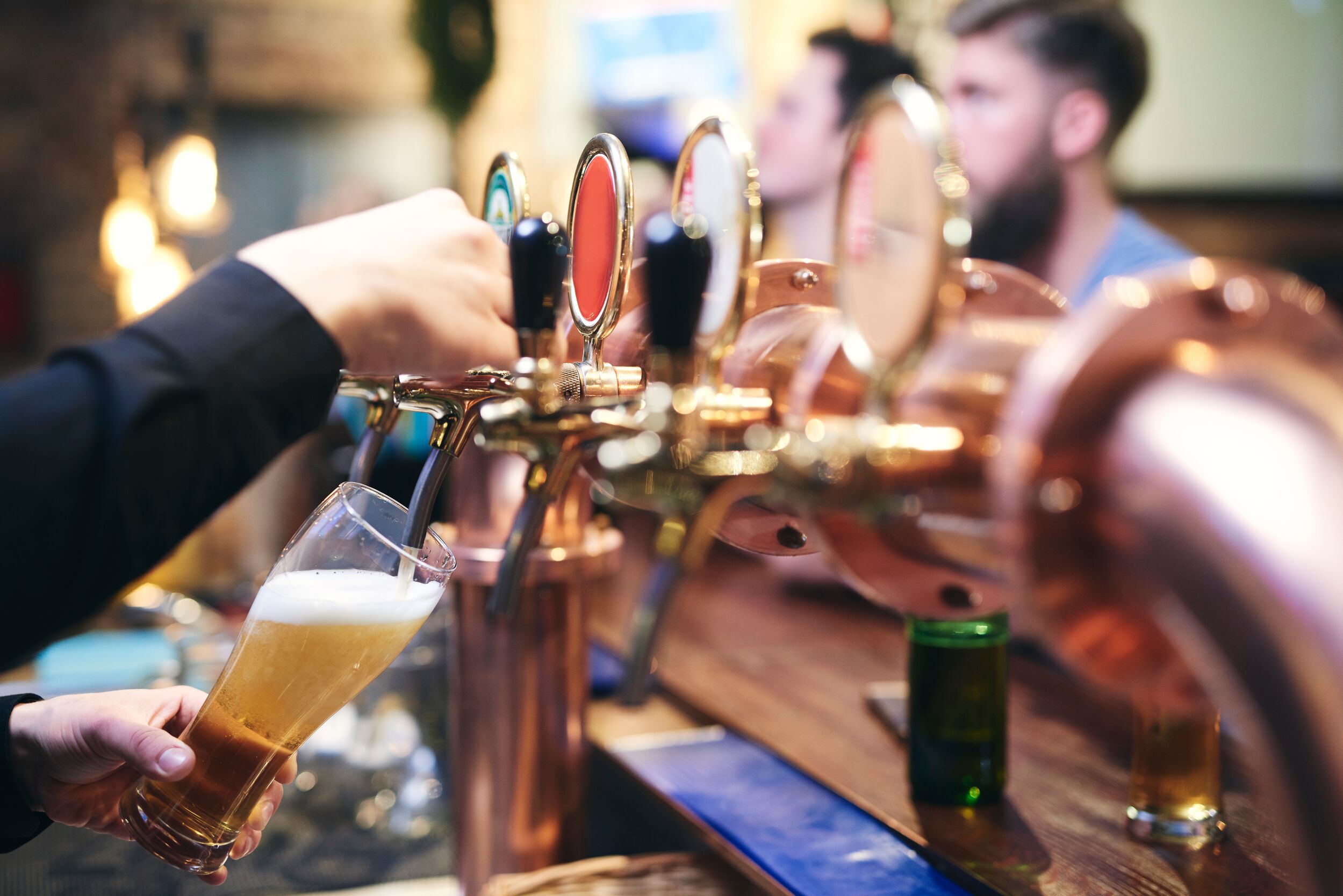 Bartender filling a glass with beer while customers sit and wait at the bar.