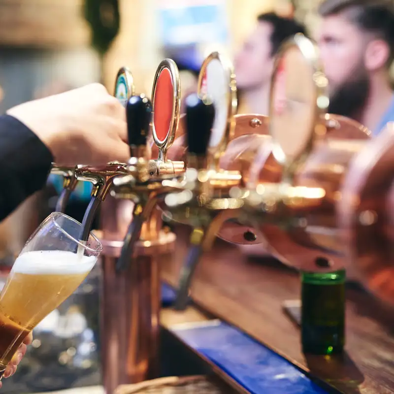 Bartender filling a glass with beer while customers sit and wait at the bar.